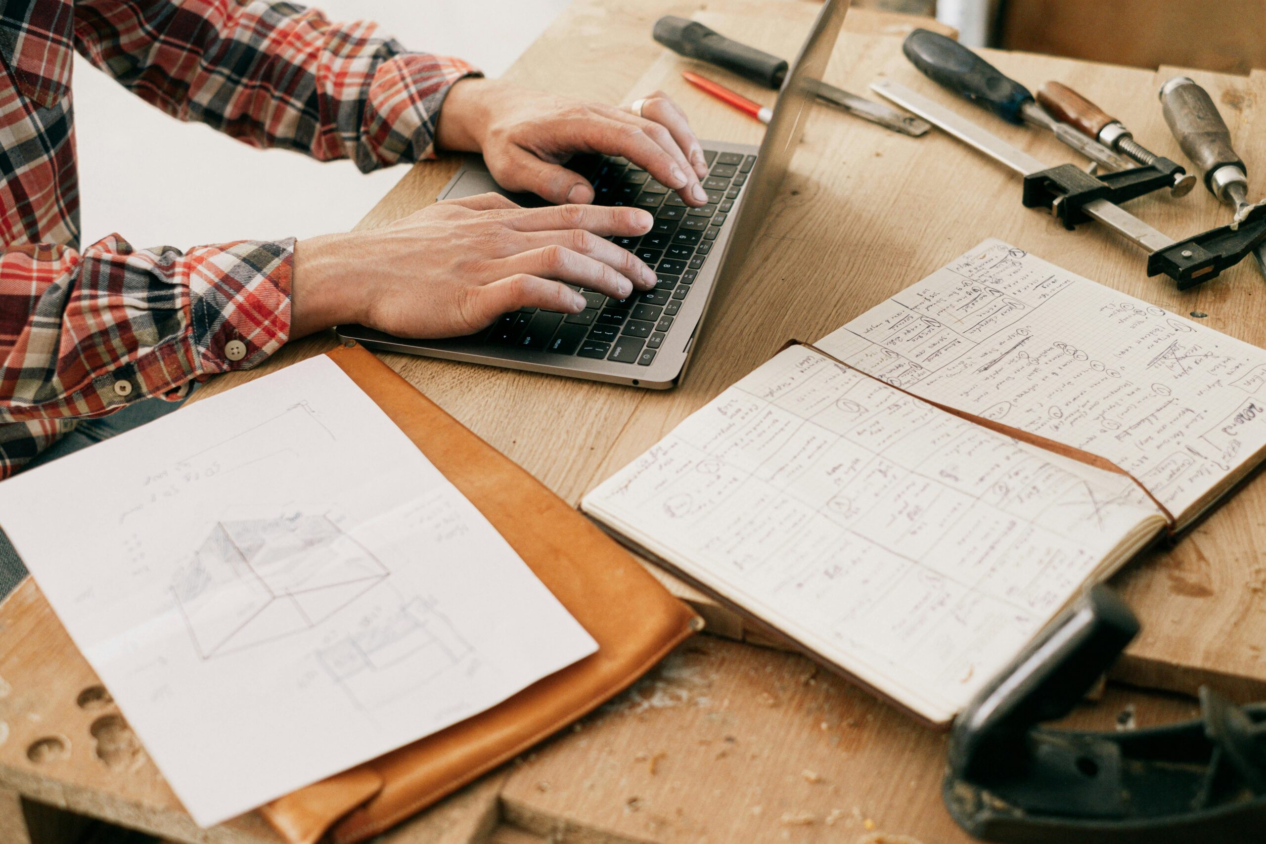 Construction contractor using payroll software on laptop in site office, managing CIS and PAYE compliance with HMRC paperwork in view.
